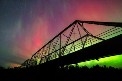 Northern lights illuminating the sky over a bridge.